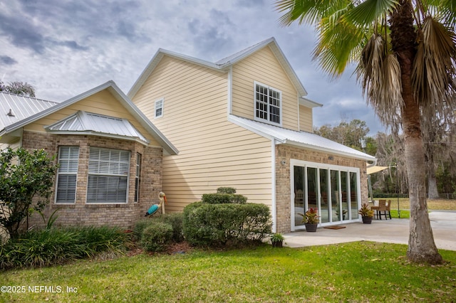 back of property with brick siding, a yard, metal roof, and a patio