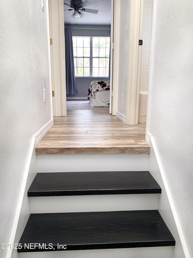 stairway with ceiling fan, wood finished floors, and a textured wall