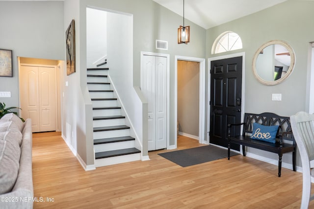 foyer featuring light wood finished floors, baseboards, visible vents, lofted ceiling, and stairs