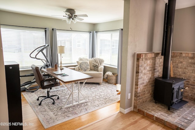 office featuring a wood stove, ceiling fan, and light wood-type flooring