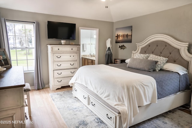 bedroom with multiple windows, ensuite bathroom, light hardwood / wood-style flooring, and vaulted ceiling