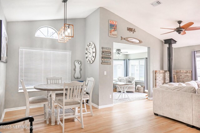 dining area with ceiling fan, wood finished floors, visible vents, baseboards, and a wood stove