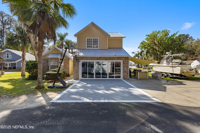 traditional-style home featuring a garage, metal roof, brick siding, and driveway