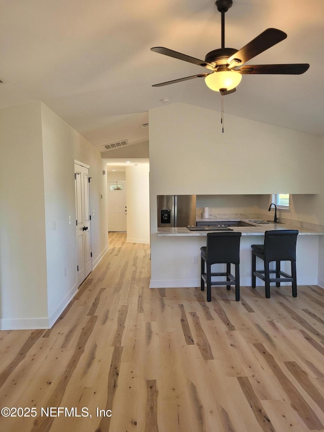 kitchen featuring kitchen peninsula, a kitchen breakfast bar, vaulted ceiling, sink, and light hardwood / wood-style floors