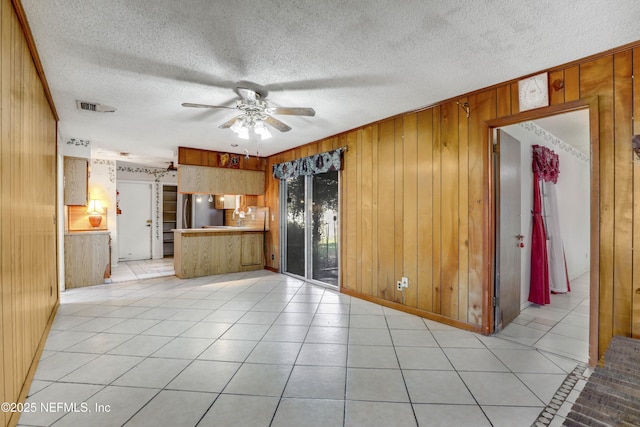 interior space featuring light tile patterned flooring, stainless steel fridge, ceiling fan, and wood walls