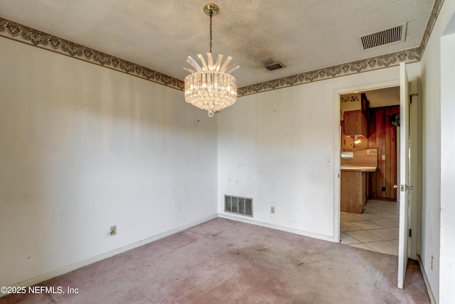 spare room with light colored carpet, a textured ceiling, and a notable chandelier