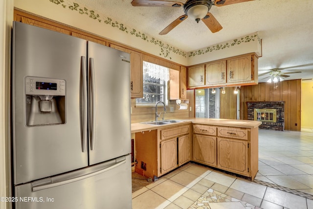 kitchen featuring sink, kitchen peninsula, stainless steel fridge, wood walls, and a textured ceiling