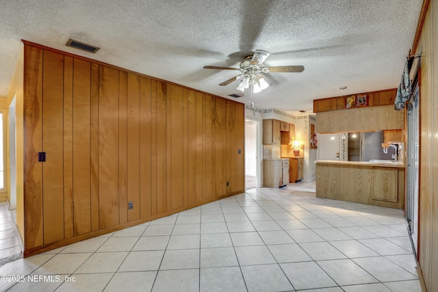 unfurnished living room featuring wood walls, sink, ceiling fan, light tile patterned floors, and a textured ceiling