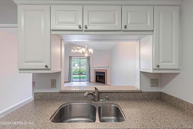 kitchen featuring light stone counters, sink, white cabinets, and a notable chandelier