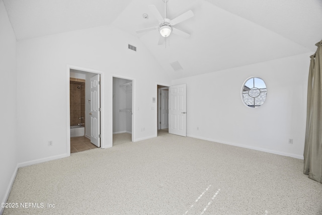 unfurnished bedroom featuring ensuite bath, ceiling fan, light colored carpet, lofted ceiling, and a walk in closet