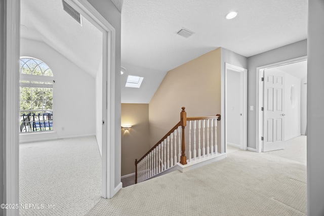 hall featuring carpet, lofted ceiling with skylight, and a textured ceiling