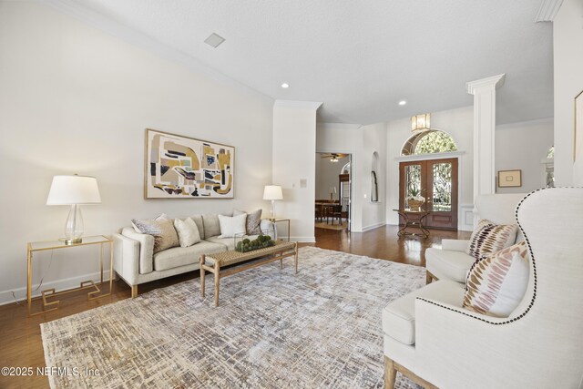 living room with ornate columns, ceiling fan, french doors, dark wood-type flooring, and crown molding