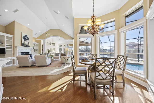 dining room featuring vaulted ceiling, hardwood / wood-style flooring, a fireplace, ceiling fan with notable chandelier, and ornamental molding