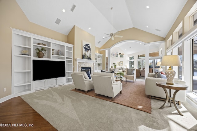 living room featuring built in shelves, ceiling fan, a high end fireplace, high vaulted ceiling, and hardwood / wood-style flooring