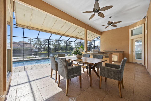 view of patio / terrace featuring ceiling fan, a water view, exterior kitchen, and glass enclosure