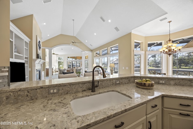 kitchen featuring light stone countertops, ceiling fan with notable chandelier, sink, hanging light fixtures, and lofted ceiling