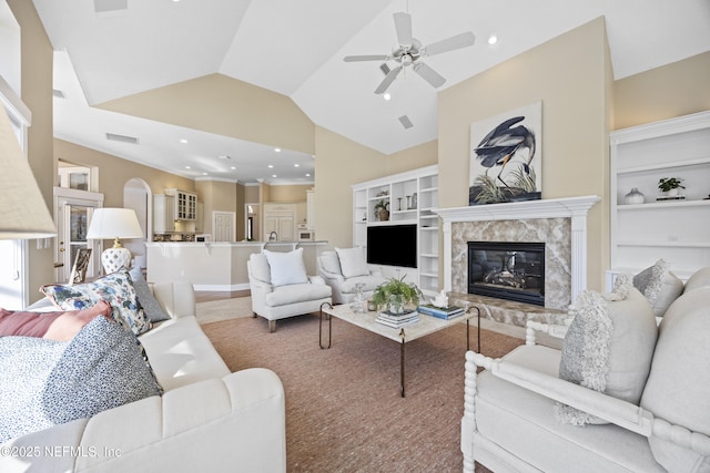 living room featuring a high end fireplace, carpet flooring, ceiling fan, built in features, and lofted ceiling