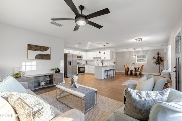 living room featuring light wood-type flooring, ceiling fan, and sink