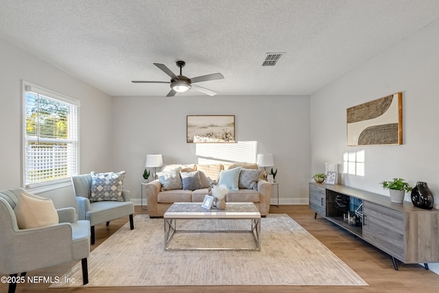 living room with ceiling fan, light hardwood / wood-style flooring, and a textured ceiling