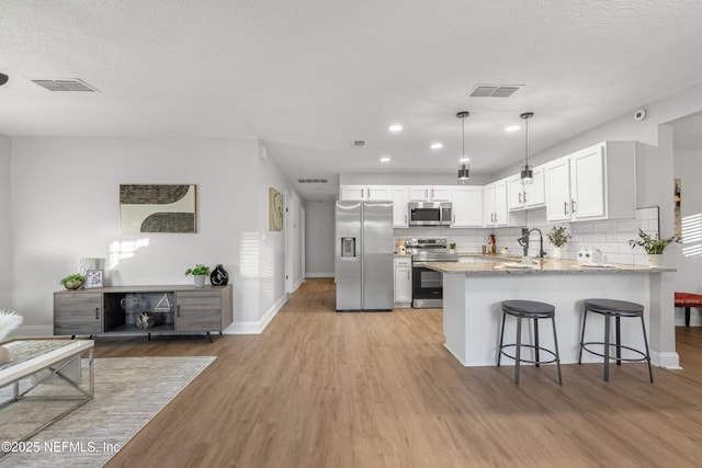 kitchen featuring light stone countertops, white cabinetry, kitchen peninsula, appliances with stainless steel finishes, and light wood-type flooring