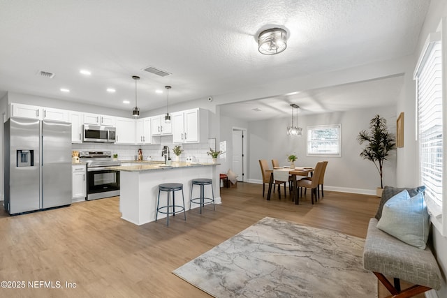 kitchen with tasteful backsplash, decorative light fixtures, a kitchen bar, white cabinets, and appliances with stainless steel finishes