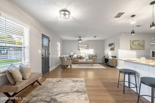 living room with ceiling fan, a textured ceiling, and light wood-type flooring