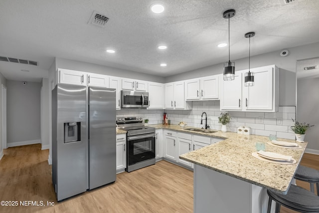 kitchen featuring sink, hanging light fixtures, a breakfast bar, white cabinets, and appliances with stainless steel finishes