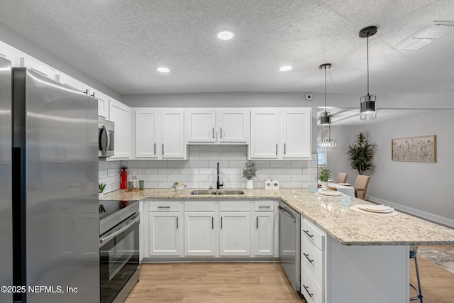 kitchen with pendant lighting, white cabinets, sink, appliances with stainless steel finishes, and kitchen peninsula