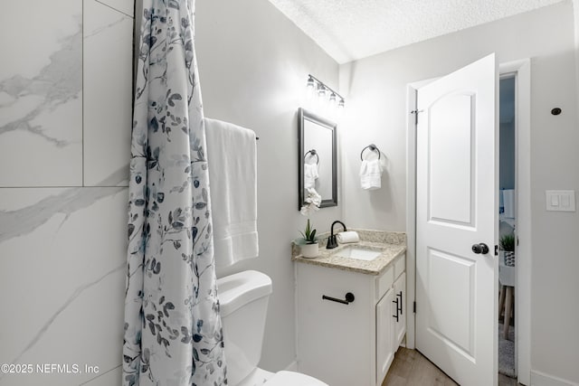 bathroom with vanity, toilet, a textured ceiling, and walk in shower