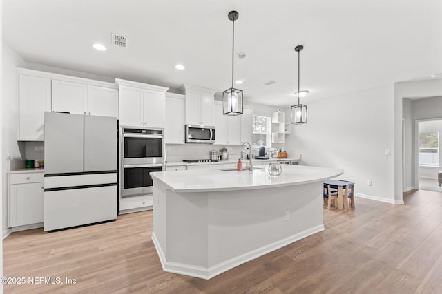 kitchen with a center island with sink, sink, decorative light fixtures, white cabinetry, and stainless steel appliances