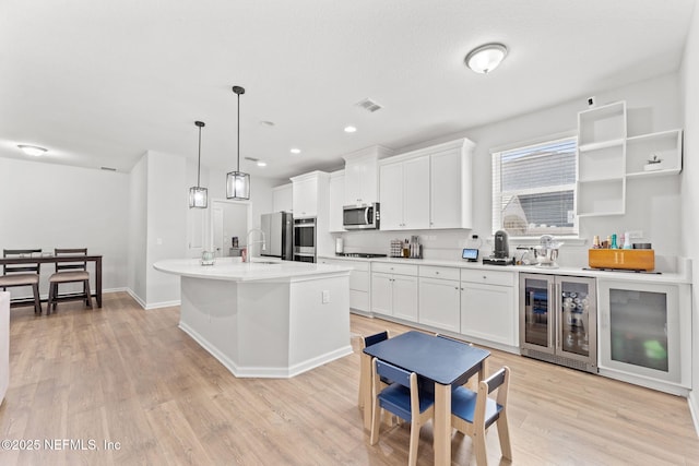 kitchen with stainless steel appliances, white cabinetry, a center island with sink, wine cooler, and hanging light fixtures