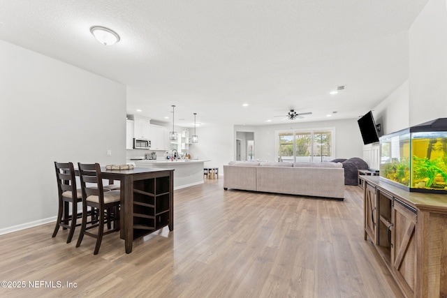 dining area featuring a textured ceiling, light wood-type flooring, ceiling fan, and sink