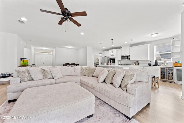 living room with light wood-type flooring, ceiling fan, and beverage cooler