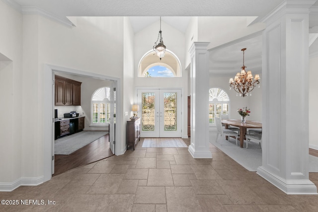 foyer entrance with a notable chandelier, ornate columns, a high ceiling, and french doors