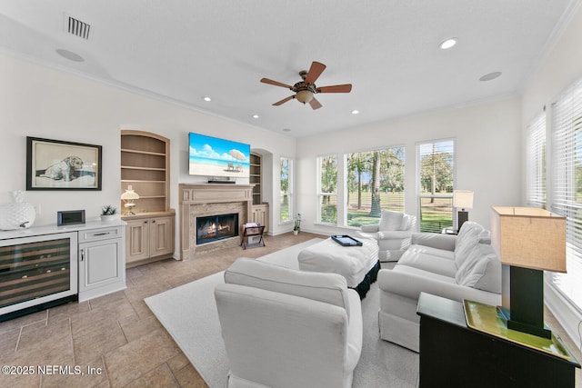 living room with ornamental molding, a textured ceiling, beverage cooler, ceiling fan, and built in features