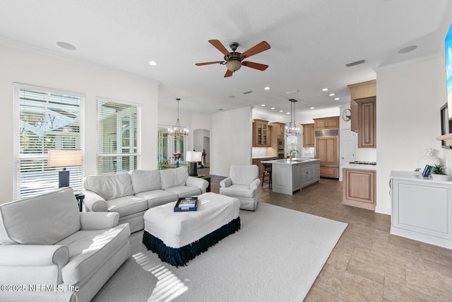 living room featuring ceiling fan with notable chandelier, crown molding, and sink