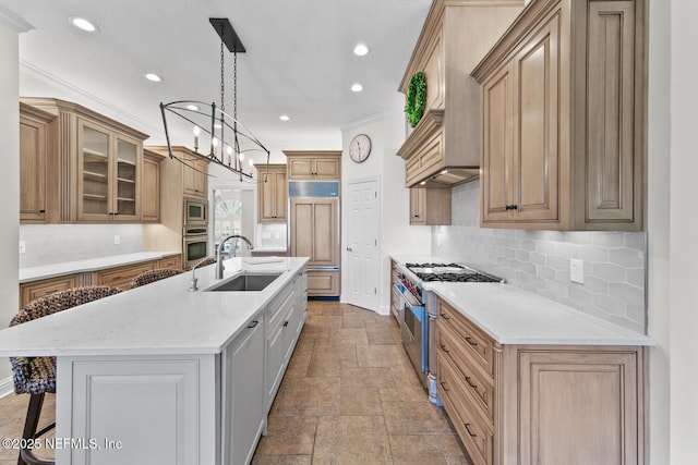 kitchen with a kitchen island with sink, sink, ornamental molding, appliances with stainless steel finishes, and a notable chandelier