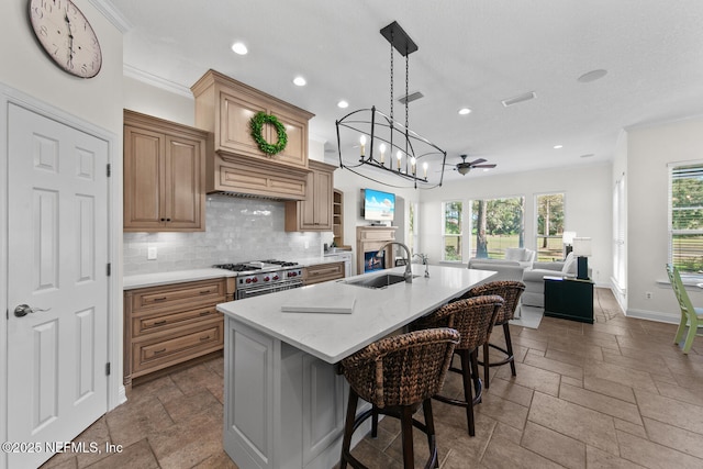 kitchen featuring sink, a large island with sink, decorative backsplash, a breakfast bar, and high end range