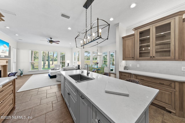 kitchen featuring ceiling fan, sink, light stone counters, backsplash, and a center island with sink