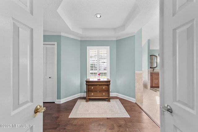 bedroom with dark hardwood / wood-style flooring, ornamental molding, a textured ceiling, a tray ceiling, and a closet