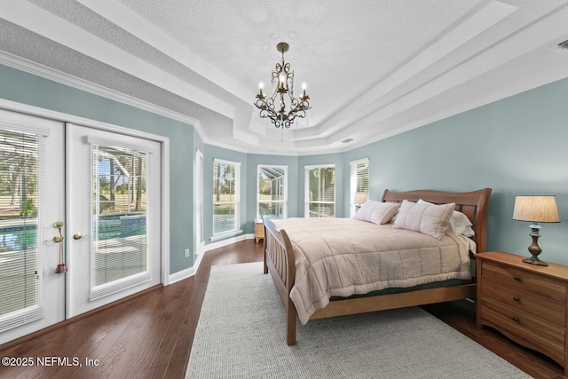 bedroom with access to exterior, dark hardwood / wood-style flooring, a chandelier, a tray ceiling, and ornamental molding