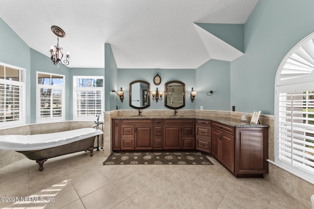 bathroom with vanity, lofted ceiling, tile patterned floors, a tub to relax in, and a notable chandelier