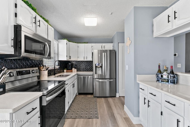 kitchen with sink, white cabinets, decorative backsplash, stainless steel appliances, and light wood-type flooring