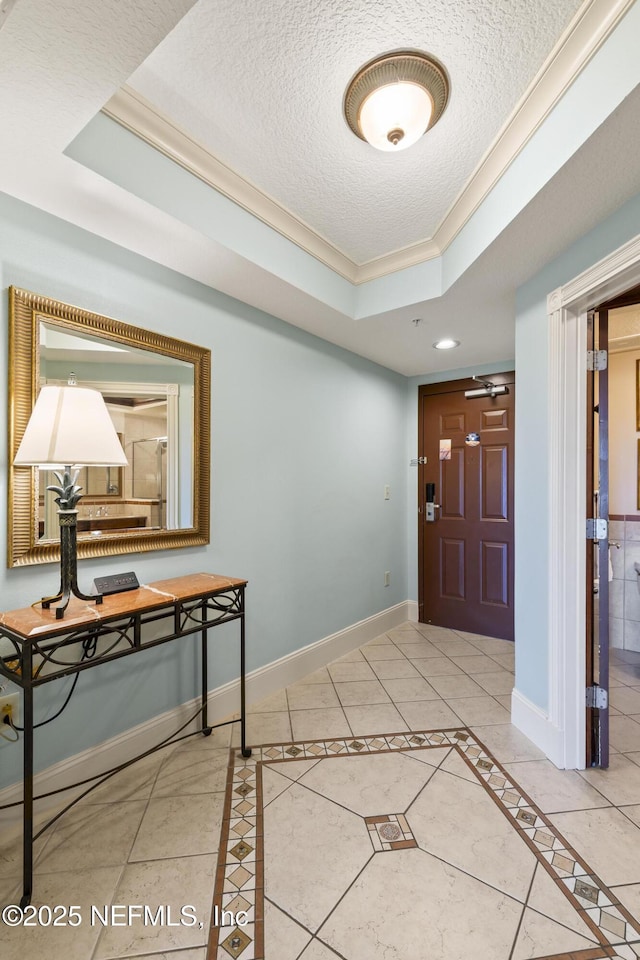 foyer with tile patterned flooring, a textured ceiling, a tray ceiling, and ornamental molding