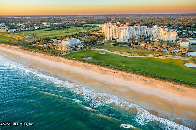 aerial view at dusk featuring a water view and a view of the beach