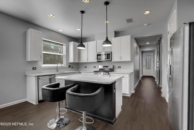 kitchen featuring dark wood-type flooring, white cabinets, pendant lighting, a kitchen island, and appliances with stainless steel finishes