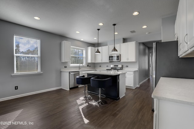 kitchen featuring appliances with stainless steel finishes, dark wood-type flooring, a center island, white cabinetry, and hanging light fixtures