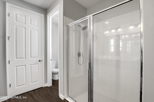 bathroom with hardwood / wood-style floors, toilet, and a shower with door