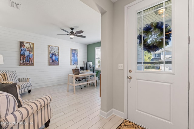 entryway featuring light wood-type flooring, plenty of natural light, wooden walls, and ceiling fan