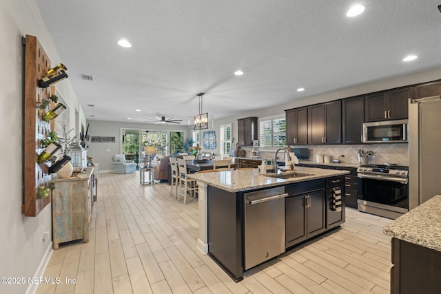 kitchen with pendant lighting, a center island with sink, sink, ceiling fan, and appliances with stainless steel finishes